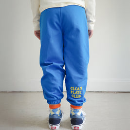 Back view of kids blue sweatpants with “Clean Plate Club” chain embroidery on the right back leg, elastic cuffs at the ankle.