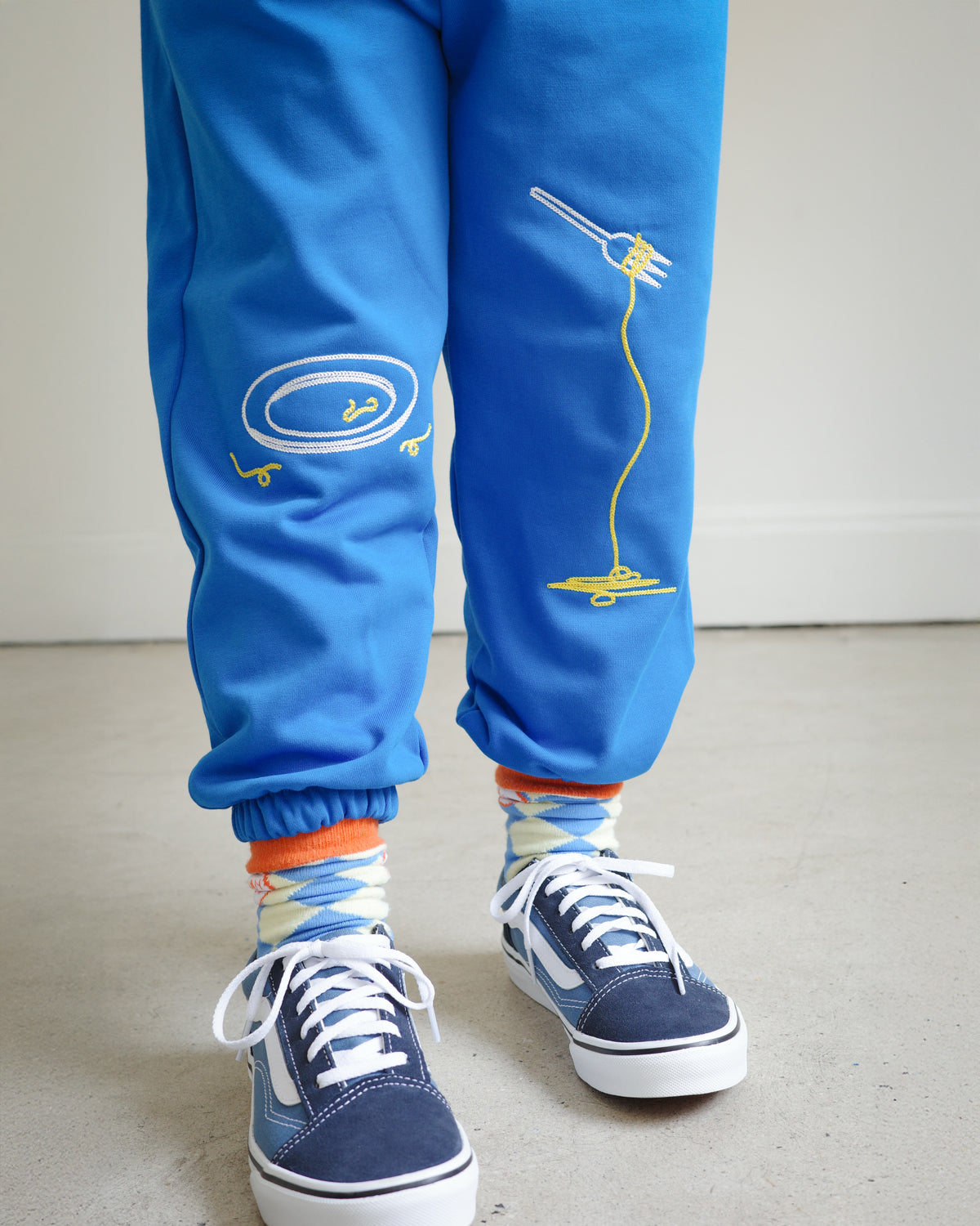 Close-up of chain embroidery on kids blue sweatpants, featuring playful food motifs: clean plate, spaghetti fork detail.