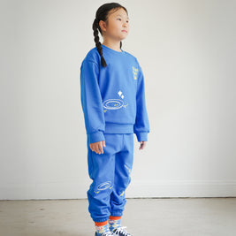 Full outfit side view of kids blue Clean Plate Club sweatshirt styled with matching embroidered sweatpants from Brrr. The sweatshirt features playful food-themed chain embroidery, including a plate motif on the front and fork and knife design on the back, combining comfort, style, and durability for everyday wear.