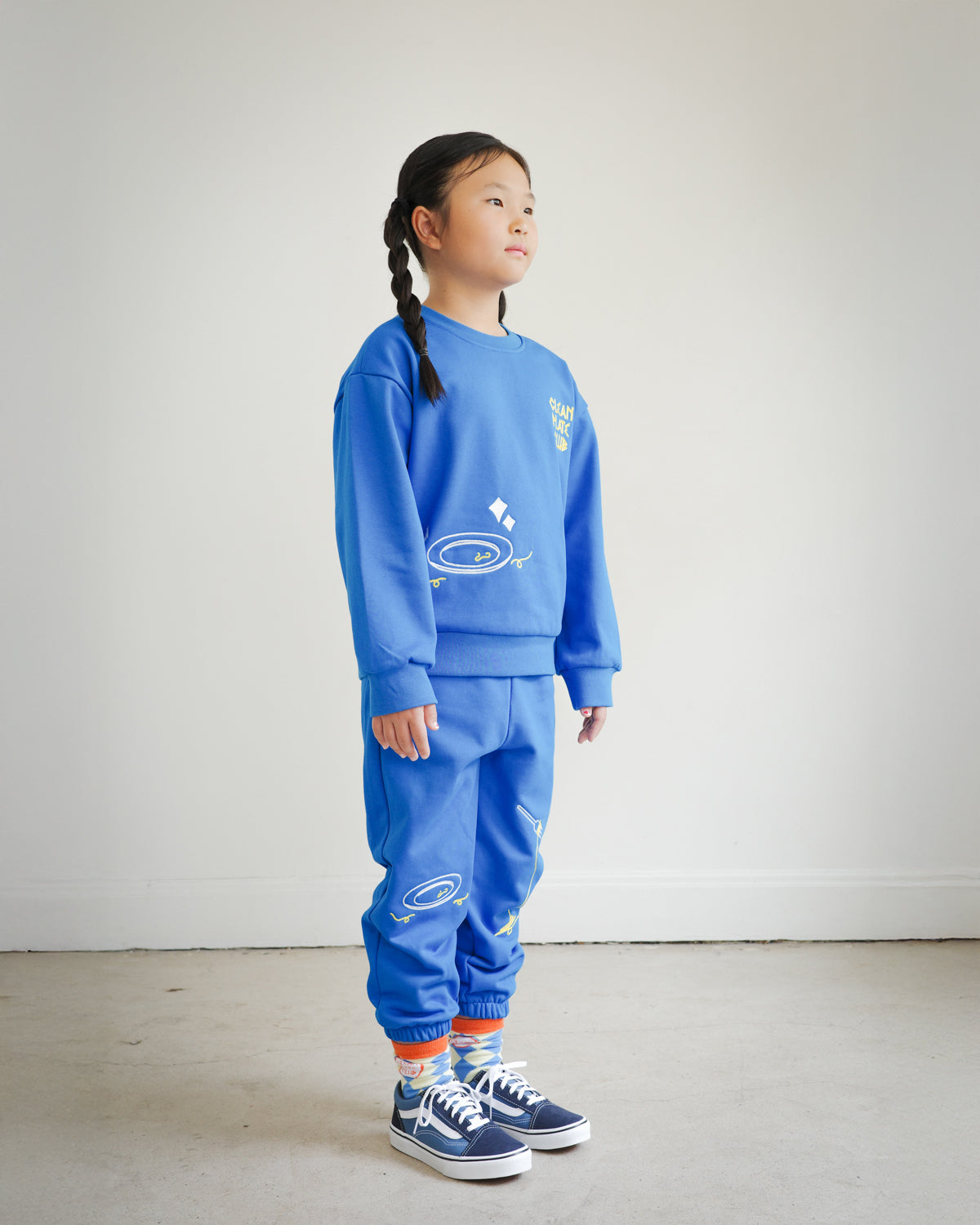 Full outfit side view of kids blue Clean Plate Club sweatshirt styled with matching embroidered sweatpants from Brrr. The sweatshirt features playful food-themed chain embroidery, including a plate motif on the front and fork and knife design on the back, combining comfort, style, and durability for everyday wear.