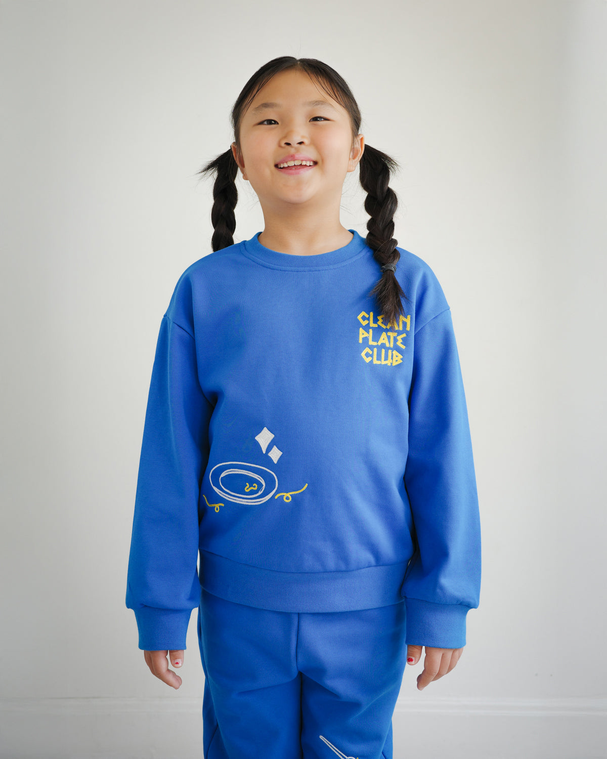 Kids blue sweatshirt by Brrr featuring Clean Plate Club embroidery, with playful chain-stitched text “Clean Plate Club” and a clean empty plate motif on the front. Designed in medium-weight cotton blend fabric for kids’ casual wear, combining comfort, durability, and a unique food-inspired design.