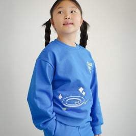 Side view of Brrr kids sweatshirt in bright blue, showcasing Clean Plate Club embroidery on the front with a plate motif. Comfortable oversized fit made with soft cotton blend, styled as part of a playful food-themed collection for children.