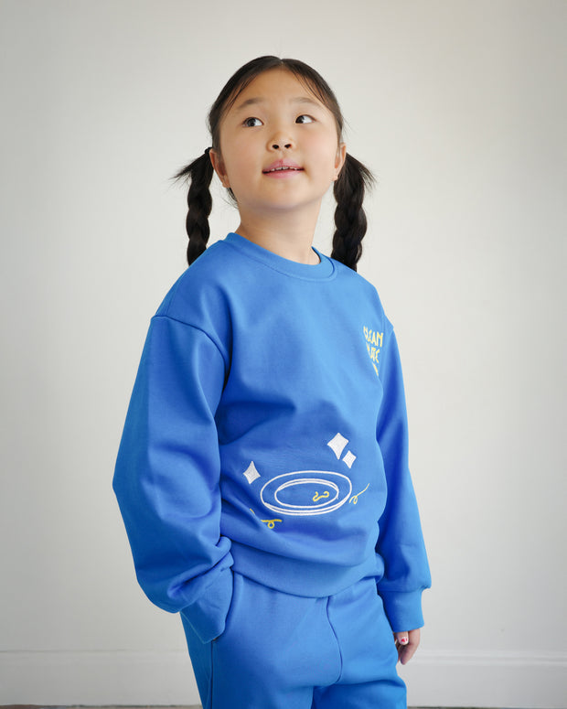 Side view of Brrr kids sweatshirt in bright blue, showcasing Clean Plate Club embroidery on the front with a plate motif. Comfortable oversized fit made with soft cotton blend, styled as part of a playful food-themed collection for children.