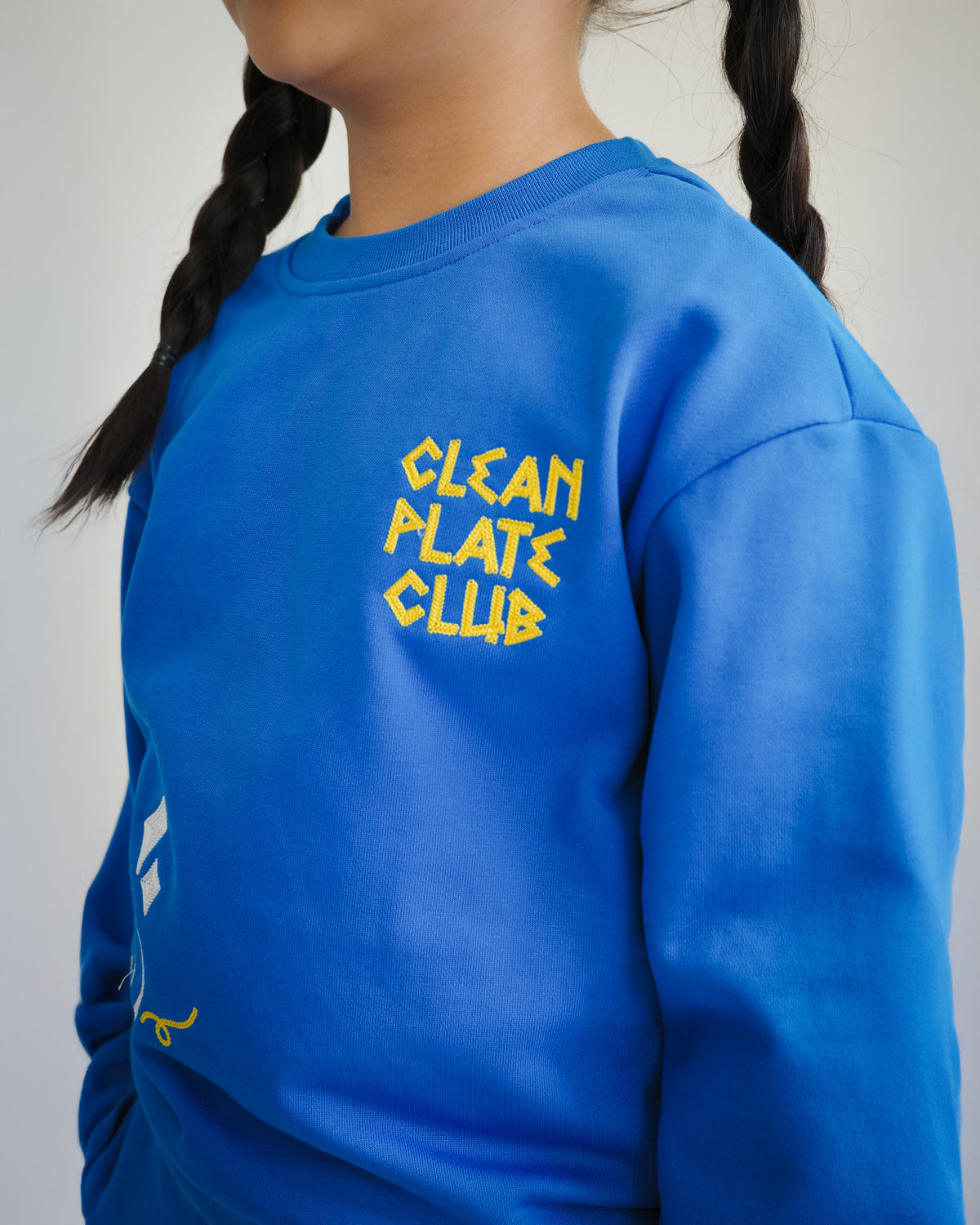 Close-up of Clean Plate Club embroidery on Brrr kids sweatshirt, highlighting chain-stitched text and food-inspired motifs. Designed in a cotton-polyester blend for comfort, this sweatshirt combines playful details with practical wearability for children.