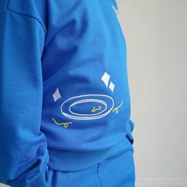 Close-up of Brrr kids blue sweatshirt from the Clean Plate Club collection, featuring chain-stitched embroidery of a clean white plate with playful yellow spaghetti details on the front. Made with a soft cotton-polyester blend, designed for comfort and durability in children’s everyday wear.