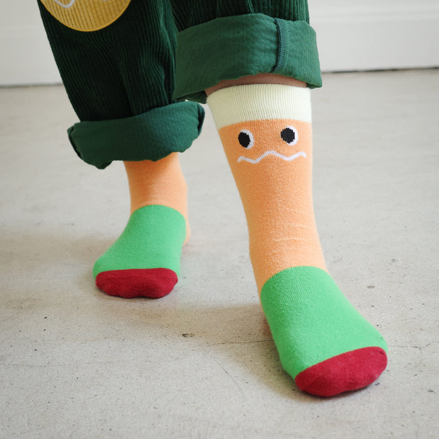 Kids Brrr Los Angeles Face color block socks featuring yellow, orange, green, and burgundy knit sections with the signature Brrr face logo on the orange ankle. Styled with green corduroy overalls, part of the Brrr kidswear collection known for playful, colorful design.
