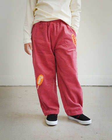 Front view of child wearing Brrr kids rose corduroy pants with corn dog embroidery on both legs, part of the Brrr Los Angeles kids clothing collection.