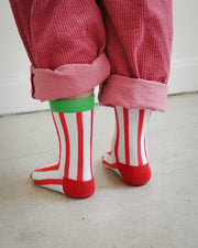 Back view of kids socks featuring red and white knit stripes with green ankle cuff and corn dog design with Brrr ketchup logo, paired with rolled-up corduroy pants