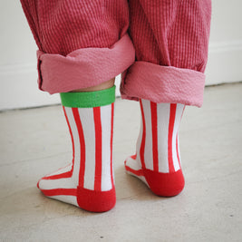 Back view of kids socks featuring red and white knit stripes with green ankle cuff and corn dog design with Brrr ketchup logo, paired with rolled-up corduroy pants