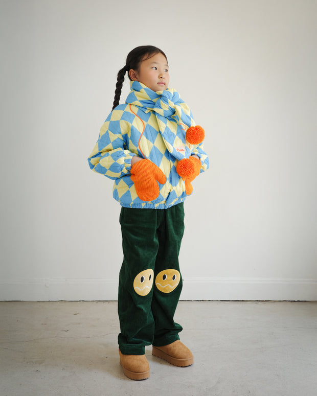 Brrr kids quilted jacket and puff scarf set in yellow and blue diamond pattern with orange mitten-shaped pockets and pompoms, designed in Los Angeles kidswear collection.