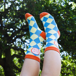 Colorful checkered socks with orange accents worn outdoors against a green tree background