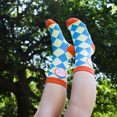 Colorful checkered socks with orange accents worn outdoors against a green tree background
