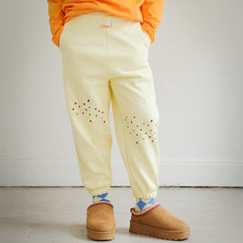 Kids yellow sweatpants from the Brrr Sweet Tooth Club collection, featuring playful food-themed chain embroidery. The front thigh is decorated with cookie crumb embroidery and an ant motif for a whimsical detail. Made with a soft cotton blend and elastic waistband for comfort in children’s everyday wear.