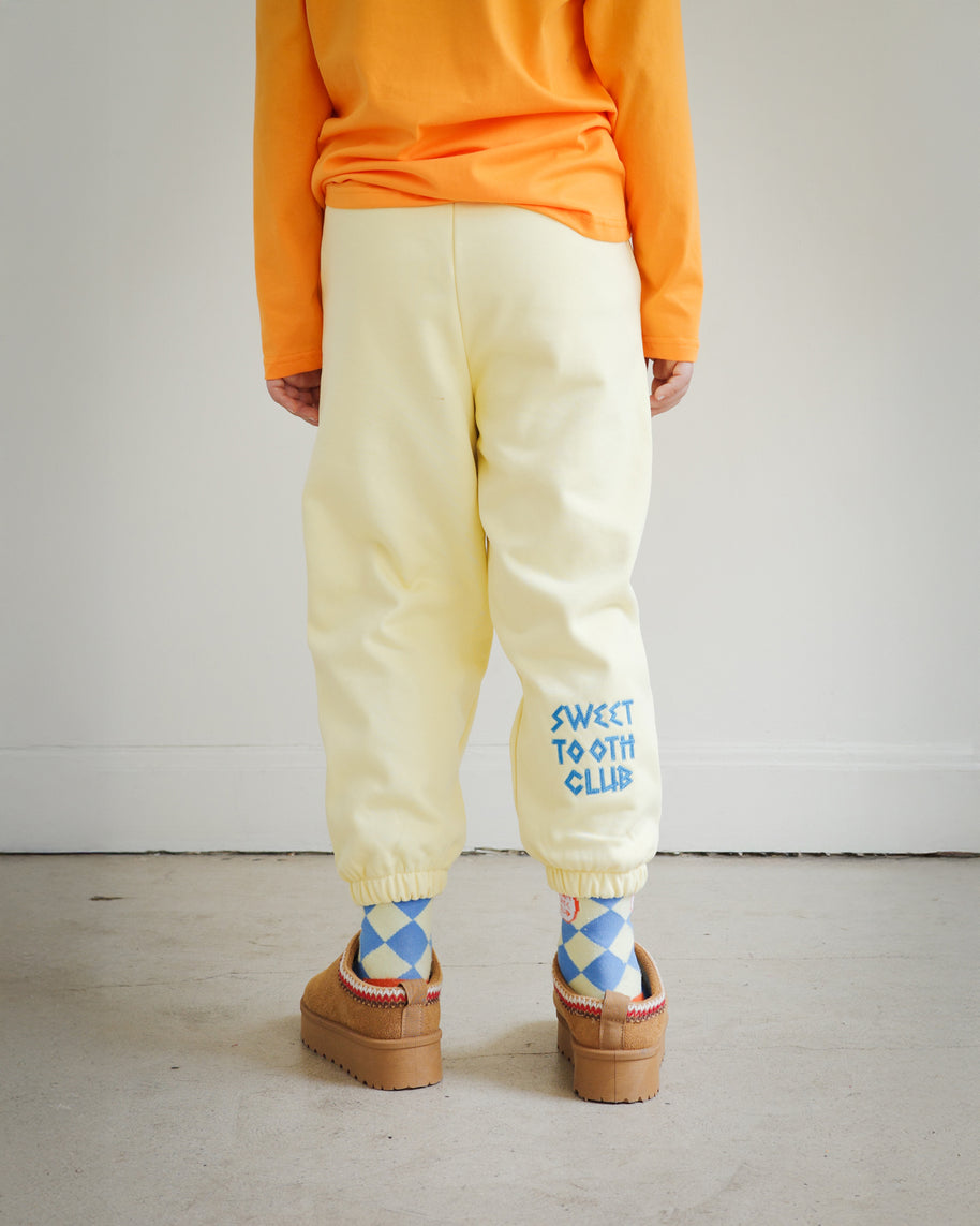 Back view of kids yellow sweatpants from Brrr, showcasing bold chain-stitched “Sweet Tooth Club” text embroidery along the back leg. Made in a medium-weight cotton blend, perfect for cooler weather children’s fashion.