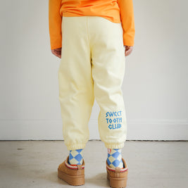 Back view of kids yellow sweatpants from Brrr, showcasing bold chain-stitched “Sweet Tooth Club” text embroidery along the back leg. Made in a medium-weight cotton blend, perfect for cooler weather children’s fashion.