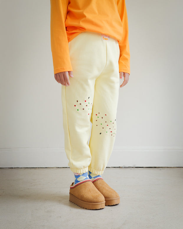 Side view of Brrr kids yellow sweatpants with cookie crumb and ant chain embroidery on the front thigh. Designed for durability and comfort, combining playful food-inspired details with a casual oversized kidswear fit.