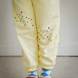 Close-up of yellow kids sweatpants with food-themed embroidery, highlighting cookie crumb and ant motifs at the front thigh and Sweet Tooth Club lettering at the back. Part of Brrr’s playful kidswear collection designed with comfort, stretch, and whimsical embroidered details.