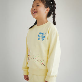 Side view of Brrr kids yellow sweatshirt with Sweet Tooth Club embroidery. Details include hot cocoa, cookie crumb and ant chain-stitched motifs on the front, made with a medium-weight cotton blend for comfort and durability in kidswear.