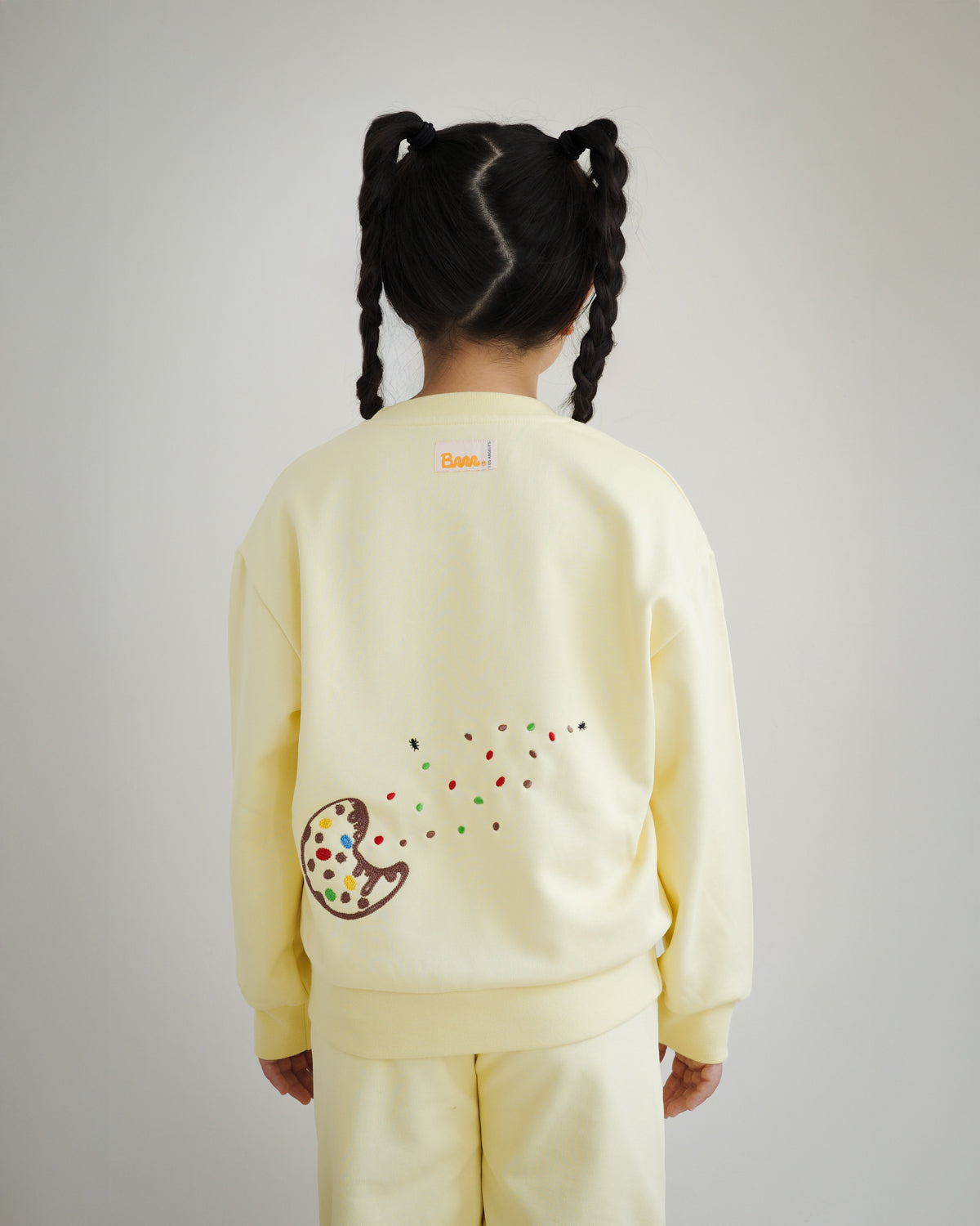 Back view of kids yellow sweatshirt by Brrr, featuring additional cookie crumb and ant chain embroidery along with playful food-inspired details. The sweatshirt combines comfort with whimsical design, reflecting the Sweet Tooth Club theme.